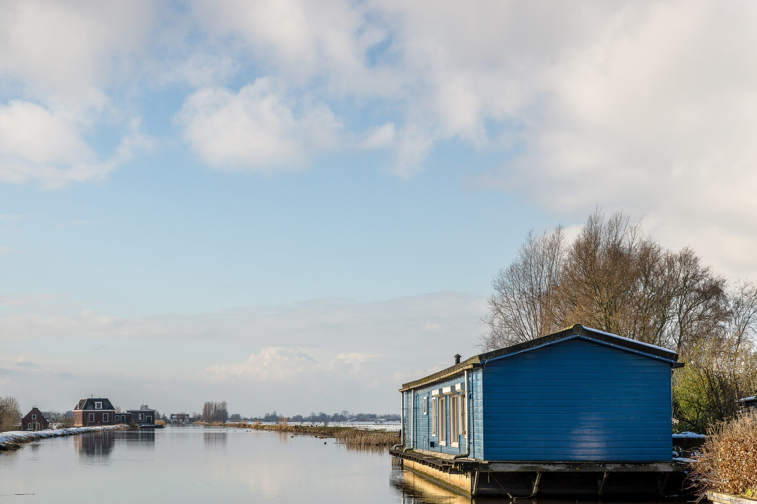 A small blue floating house over the water with buildings in the distance under a blue sky for minimalist house ideas. 